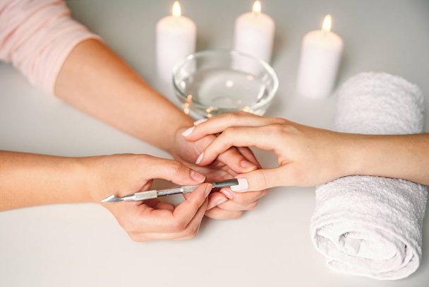 Nail care. Closeup of beautiful woman hands getting manicure in spa salon. Female manicurist cleaning cuticle with professional manicure pusher tool. Cosmetic procedure. - Zdjęcie, obraz