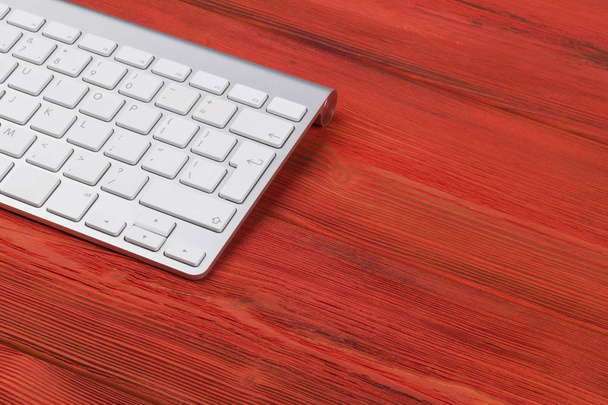 Close up view of a business workplace with wireless computer keyboard, keys on old red natural wooden table background. Office desk with copy space - Foto, afbeelding