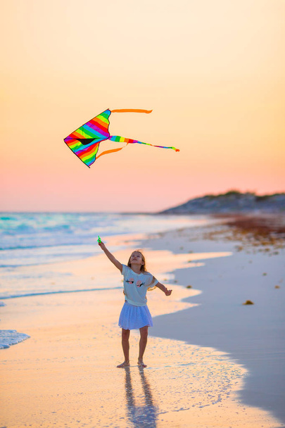 Petite fille avec cerf-volant volant sur la plage tropicale au coucher du soleil. Un gamin joue au bord de l'océan. Enfant avec jouets de plage
. - Photo, image