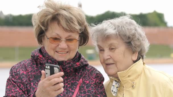 Woman shows photo to old woman using mobile phone - Séquence, vidéo