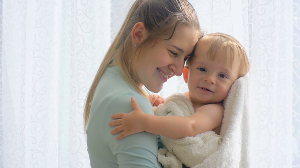 Slow motion beelden van moeder met schattige baby in de handdoek knuffelen op groot venster - Video
