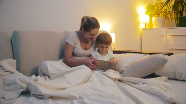 Beautiful mother with baby boy playing games on tablet before going to sleep - Footage, Video