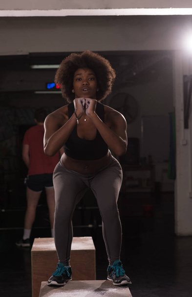 black female athlete is performing box jumps at gym - Photo, Image