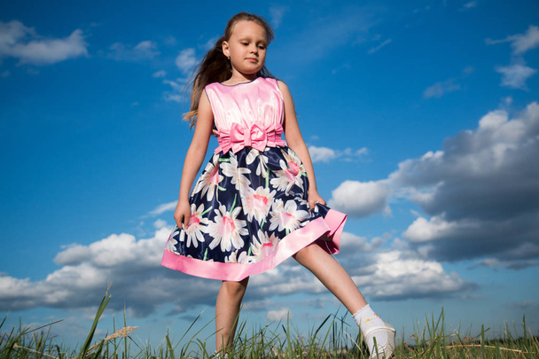 Portrait of a seven year old girl in a bright pink dress on the grass in the park - 写真・画像