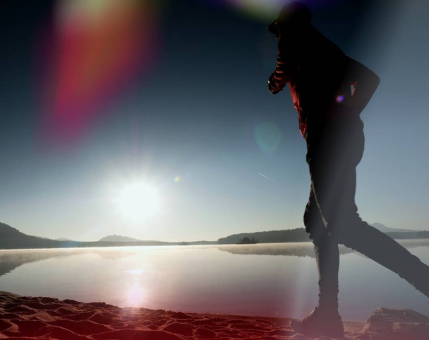 Витік світла в лінзі. Високий стрункий чоловік тренується на пляжі гірського озера
. - Фото, зображення