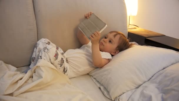 4k footage of adorable baby boy lying in bed and holding digital tablet - 映像、動画