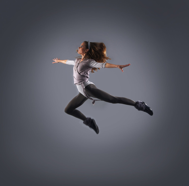 Young, attractive, sporty and sexy modern dancer jumping over grey background - Photo, Image