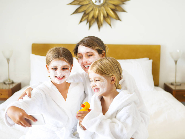 Feliz madre y niñas en batas de baño en la cama
 - Foto, imagen