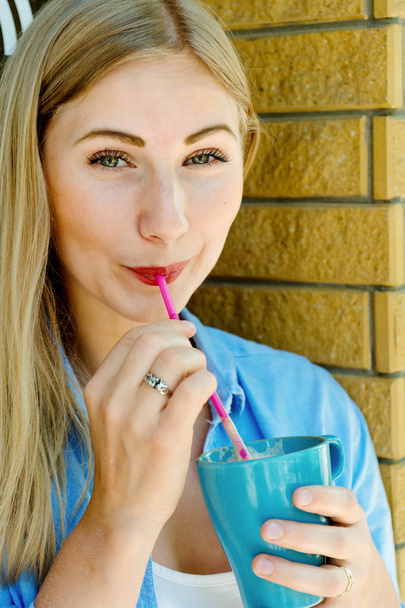 Young and beautiful blonde girl drinking cappuccino and looking into camera. Portrait of attractive cute woman - Photo, Image