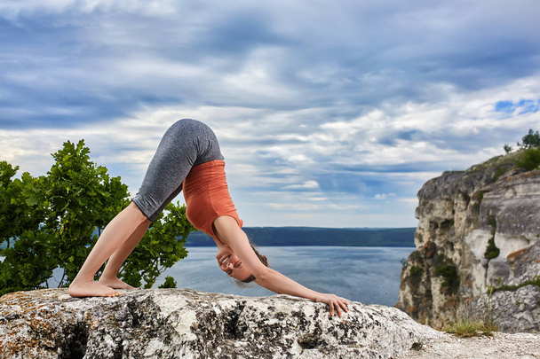 Attractive woman standing on the rock and doing yoga exercises above river. - Foto, Bild