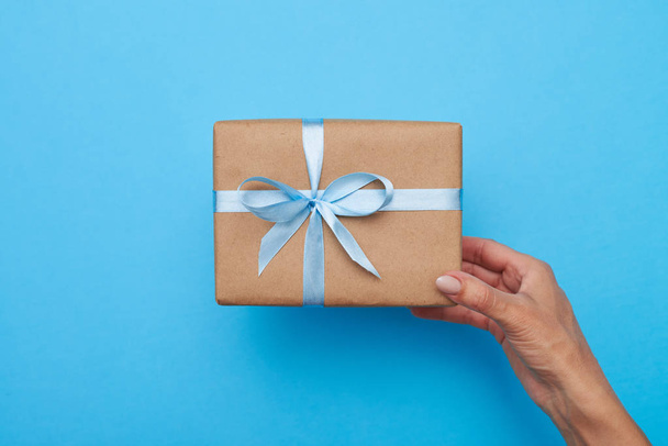 Руки женщины с подарочной коробкой на синем фоне
  - Фото, изображение