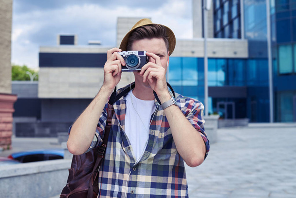 Verblüffter junger Mann mit Kamera macht Fotos in der Innenstadt  - Foto, Bild
