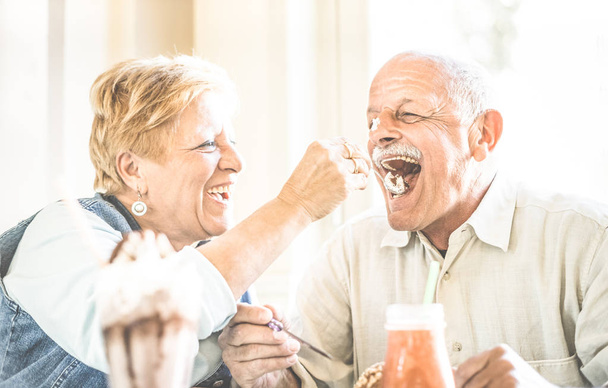 Gelukkige voormalig senior paar verliefd genieten van bio icecream cup - vreugdevolle ouderen levensstijl concept - vrouw voeding echtgenoot en plezier op bar café restaurant tijdens de groenblijvende vakantie - Retro filter - Foto, afbeelding