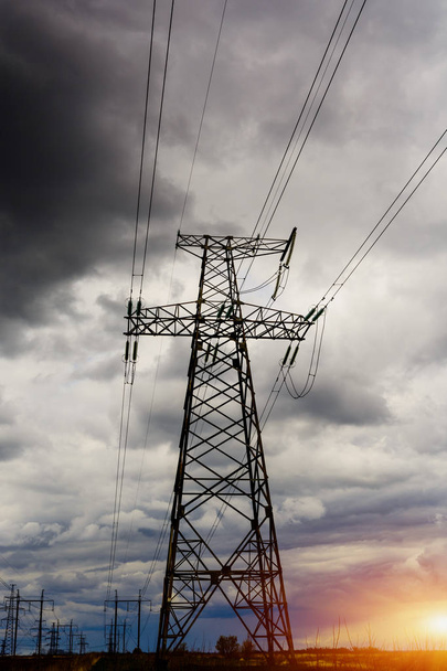 Sähkö Power Lines venyttää poikki rypsipellon auringonlaskun alla myrskyinen näköinen taivas
. - Valokuva, kuva