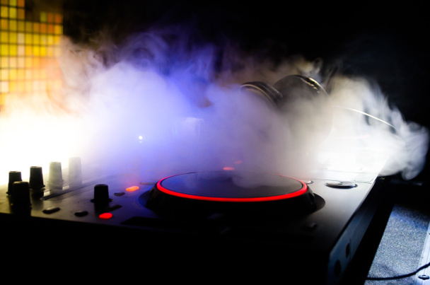 DJ spinnen, mixen en scratchen in een nachtclub, handen van dj tweak verschillende track besturingselementen op dj's dek, strobe lights en mist, selectieve aandacht - Foto, afbeelding