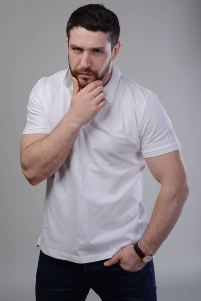 Puzzled bearded young man stroking touching beard looking at camera - Photo, Image