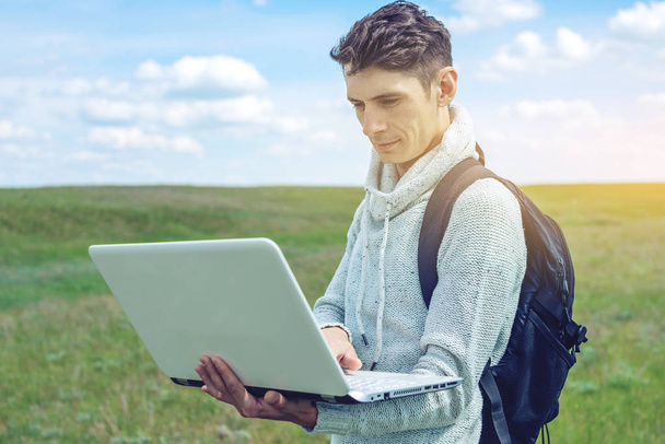 Jovem sentado em um prado verde com laptop sem fio no fundo do céu azul nublado
 - Foto, Imagem