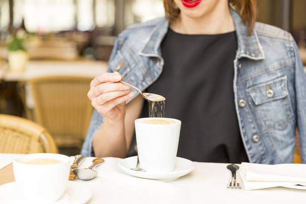 schönes junges Mädchen, das sich in einem Café ausruht und dem Kaffee Zucker hinzufügt - Foto, Bild