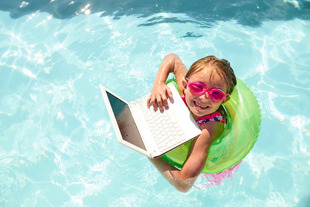 Joyful little girl swimming in pool with laptop - Foto, afbeelding