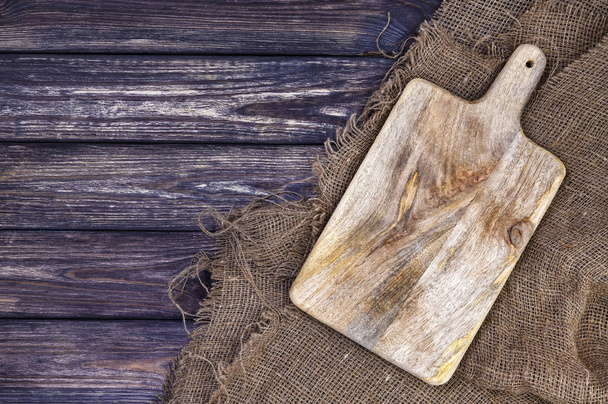 Old chopping board on dark wood background, cutting tray over burlap tablecloth, top view - Foto, Imagem