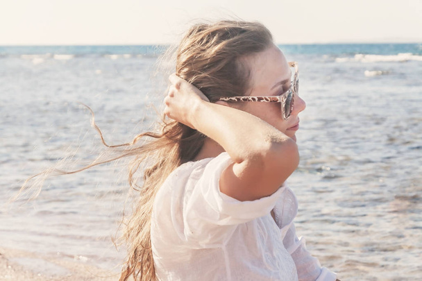 eine junge Frau mit Sonnenbrille hält eine Hand vor ihr flatterndes Haar  - Foto, Bild