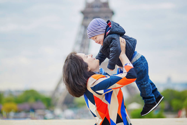 Mother throwing her little son in the air near the Eiffel tower - Фото, изображение