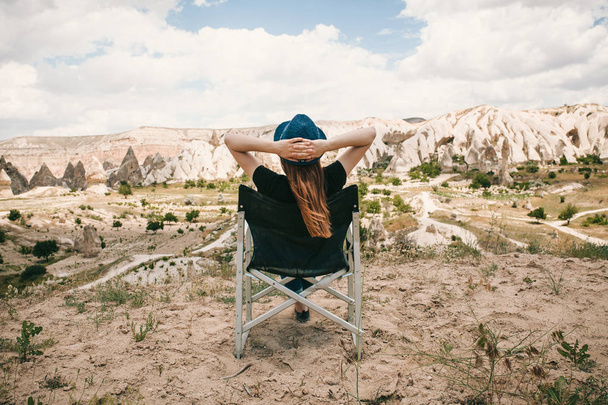 Kız bir sandalyede oturur, rahatlatır ve Türkiye'de Kapadokya'nın eteklerindeki muhteşem bir görünüm hayran. Gevşeme, dinlenme, tatil, seyahat. - Fotoğraf, Görsel