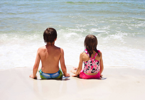 Rear view of little children sitting on beach - Valokuva, kuva