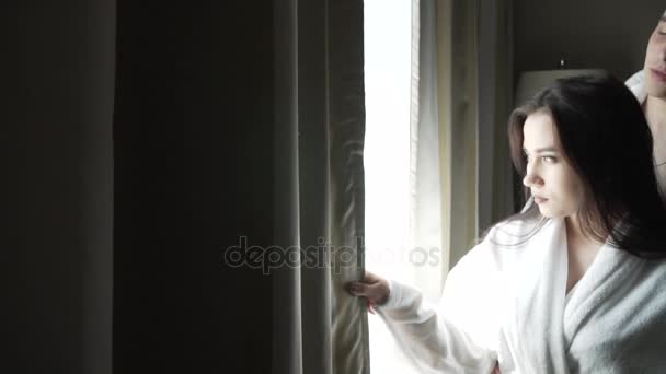 Loving couple in white coats looks at the landscape outside window and kisses stock footage video - Footage, Video