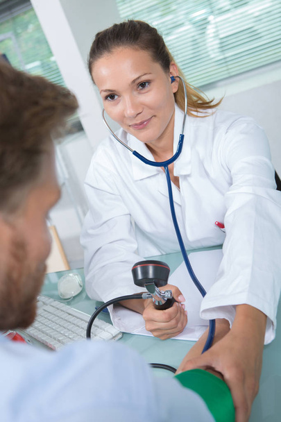 female doctor measuring blood pressure of man in hospital - Foto, afbeelding