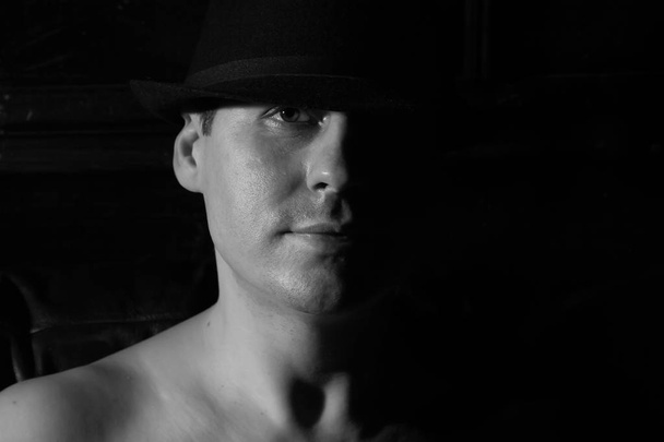 Man in a black hat with naked shoulders. Black and white. - Foto, Imagen