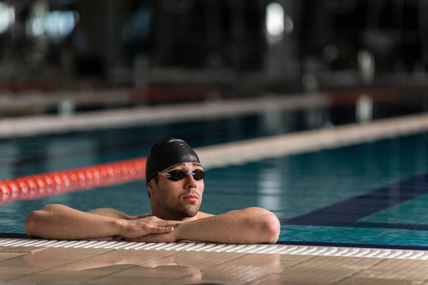Male swimmer wearing goggles and swimming cap resting - Zdjęcie, obraz