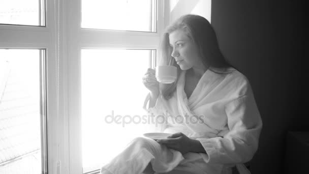 4k black and white video of beautiful woman drinking coffee on windowsill - Footage, Video