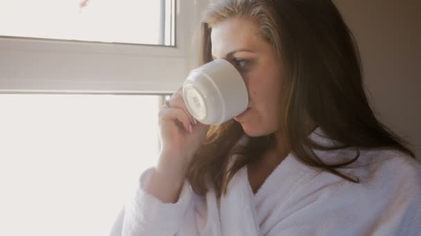 4 k closeup video pencerede kahve içme bornoz içinde güzel genç kadın - Video, Çekim