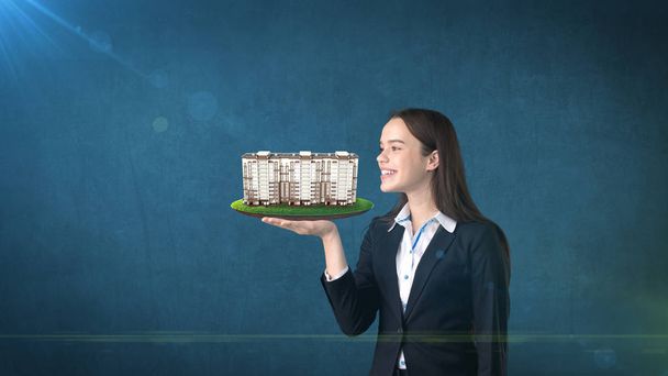 Young woman holding modern condominium on the open hand palm, over isolated studio background. Business concept. - Foto, Imagem