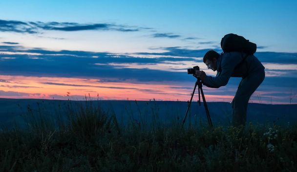 Silhouette eines professionellen Fotografen mit einem Stativ, der ein Foto macht  - Foto, Bild