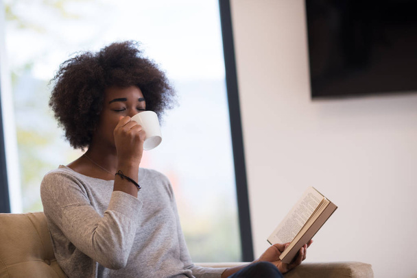 black woman reading book  in front of fireplace - Photo, Image