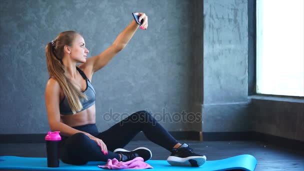 Een jong meisje met een goed figuur maakt selfie op een mobiele telefoon in de sportschool - Video