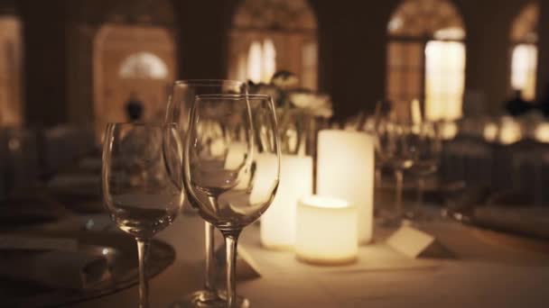 Leere Weingläser auf dem Tisch mit brennenden Kerzen und Tellern im Festsaal - Filmmaterial, Video