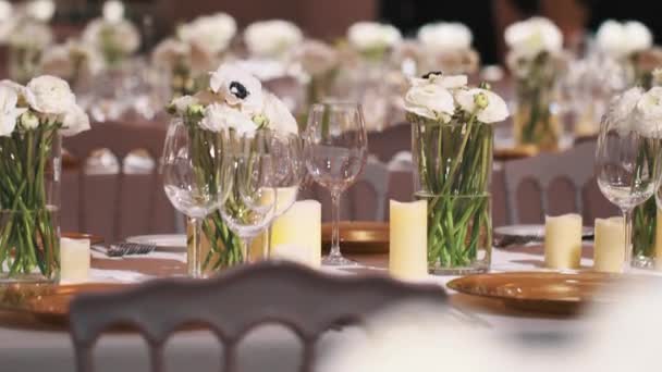 Reihen von Weingläsern und weißen Blumen in Vasen auf Esstischen beim Bankett - Filmmaterial, Video
