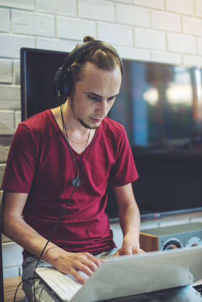 Young man in headphones listens to music and works at a laptop in a multimedia atmosphere - Photo, Image