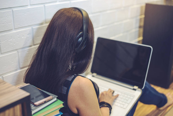 Chica con auriculares escuchando lecciones o audiolibros en el teléfono y trabajando en el ordenador portátil. Concepto de educación tecnológica
 - Foto, Imagen