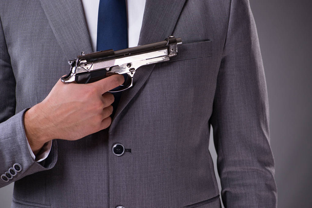 Бізнесмен витягує пістолет з кишені
 - Фото, зображення
