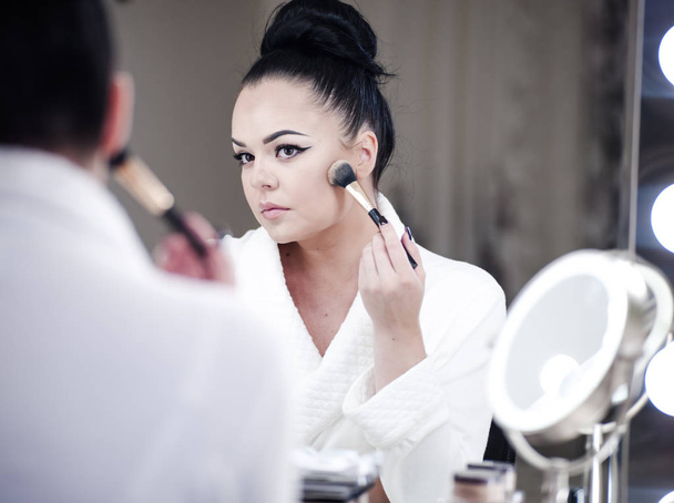 Portrait of a brunette woman putting on make up in front of the mirror - Foto, Bild