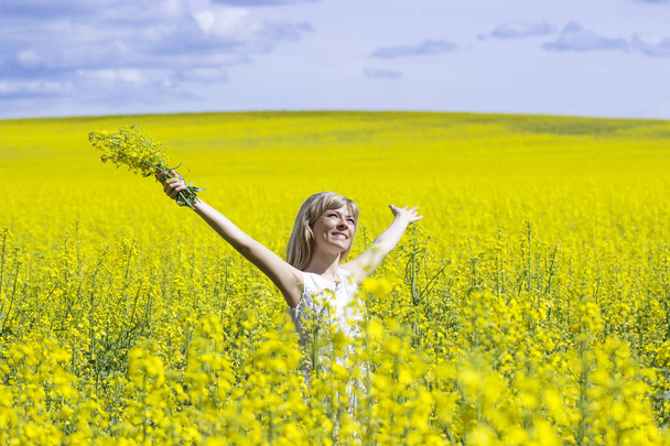 Woman with long hair standing on yellow rapeseed meadow with raised hands. Concept of freedom and happiness. - Foto, immagini