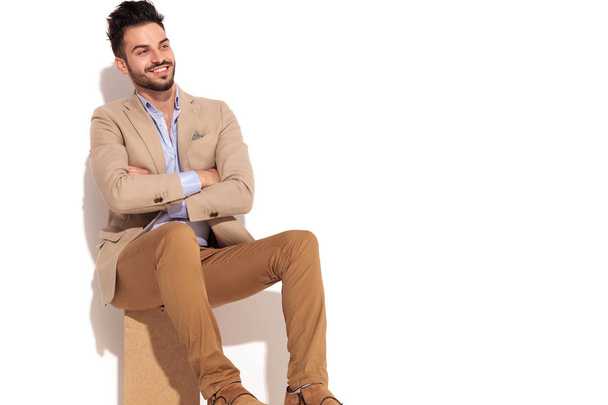 Сидящий молодой бизнесмен, сидящий со скрещенными руками, смотрит в сторону
 - Фото, изображение