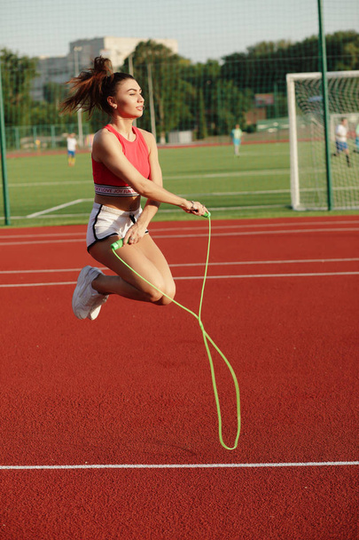 Young cute fitness female. Attractive sporty woman jumping on skipping rope in stadium, healthy lifestyle concept. - Φωτογραφία, εικόνα