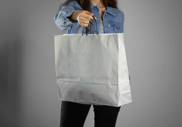 The girl in the blue denim shirt holding blank clean paper bag.  - Foto, afbeelding