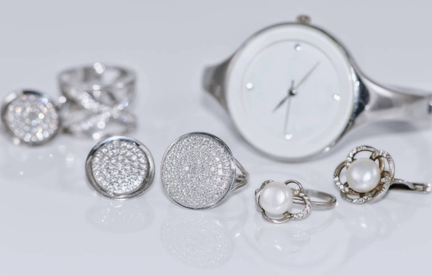 Ασημένια δαχτυλίδια και σκουλαρίκια στο φόντο των ρολόγια - Φωτογραφία, εικόνα
