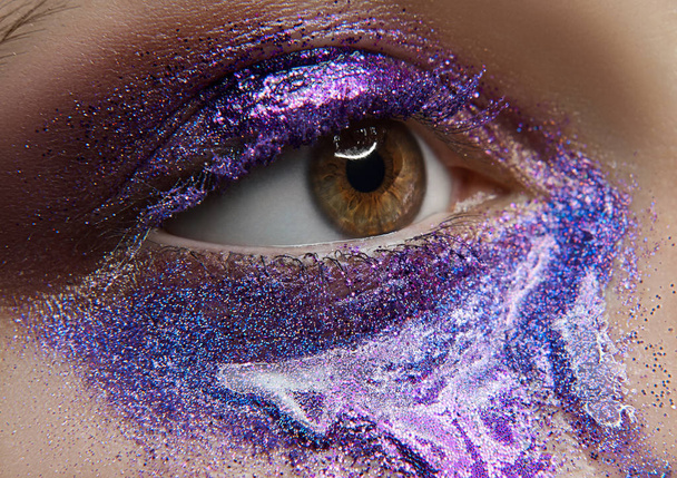Macro and close-up creative make-up theme: beautiful female eye with purple pigment and sequins, retouched photo - Фото, изображение